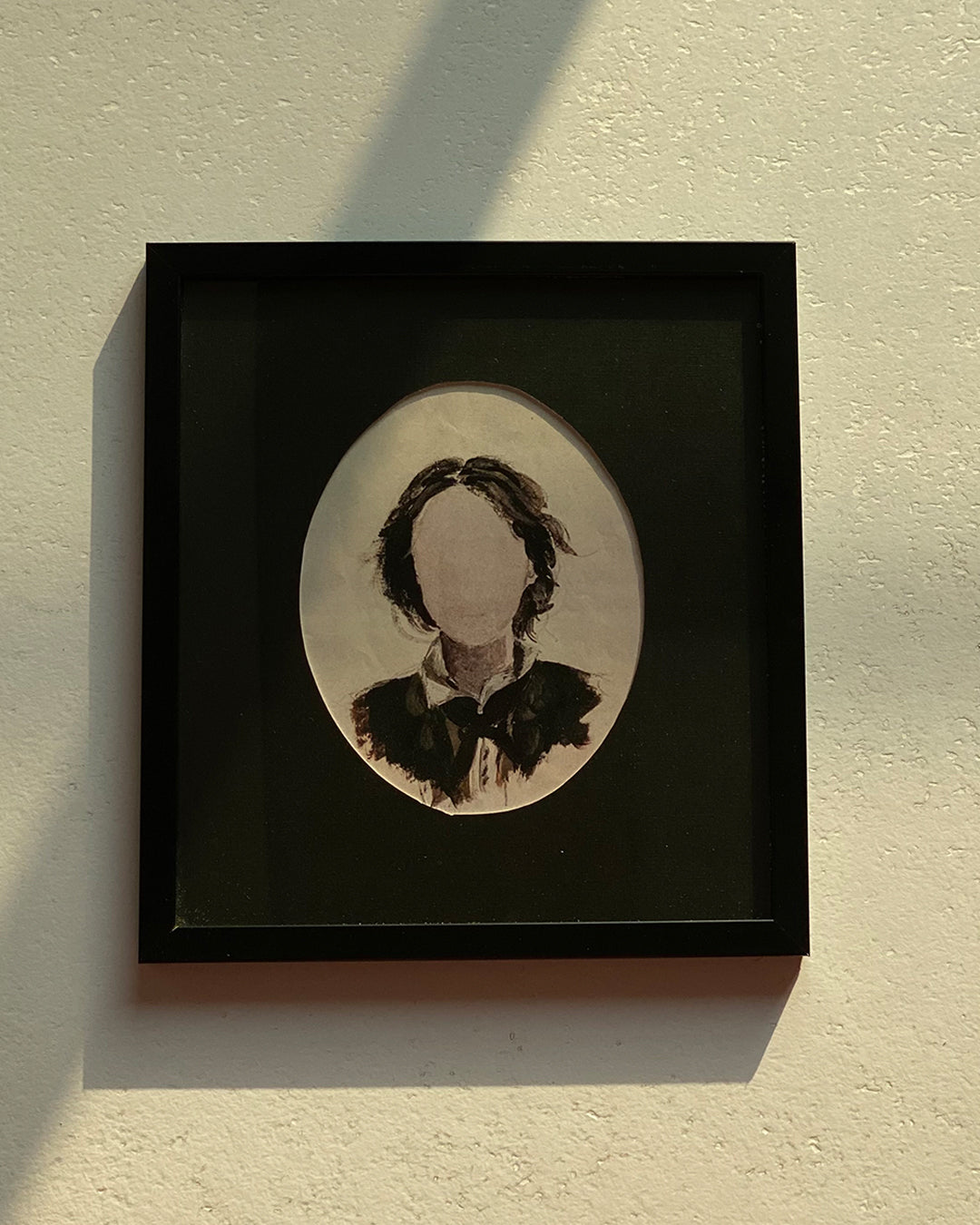 Framed portrait painting in a black frame displayed on a beige wall